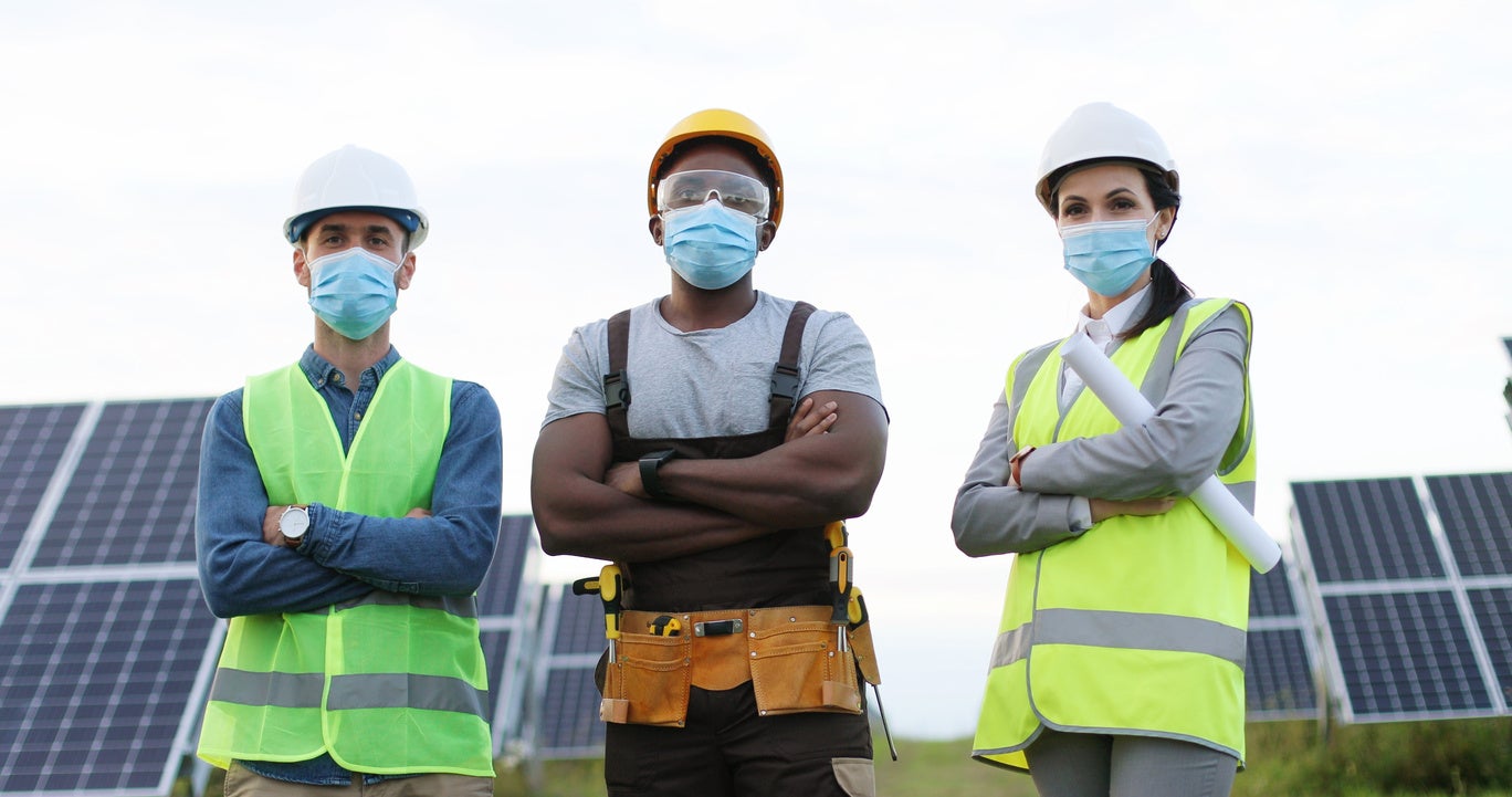 Group of multiethnic engineers in medical protective mask on background of photovoltaic solar panels.