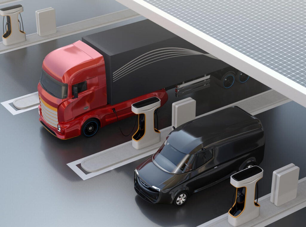 Generic design Heavy Electric Trucks charging at Public Charging Station with roof-mounted solar panels. 3D rendering image.