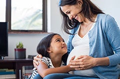 Young child feeling pregnant woman's stomach, both smiling