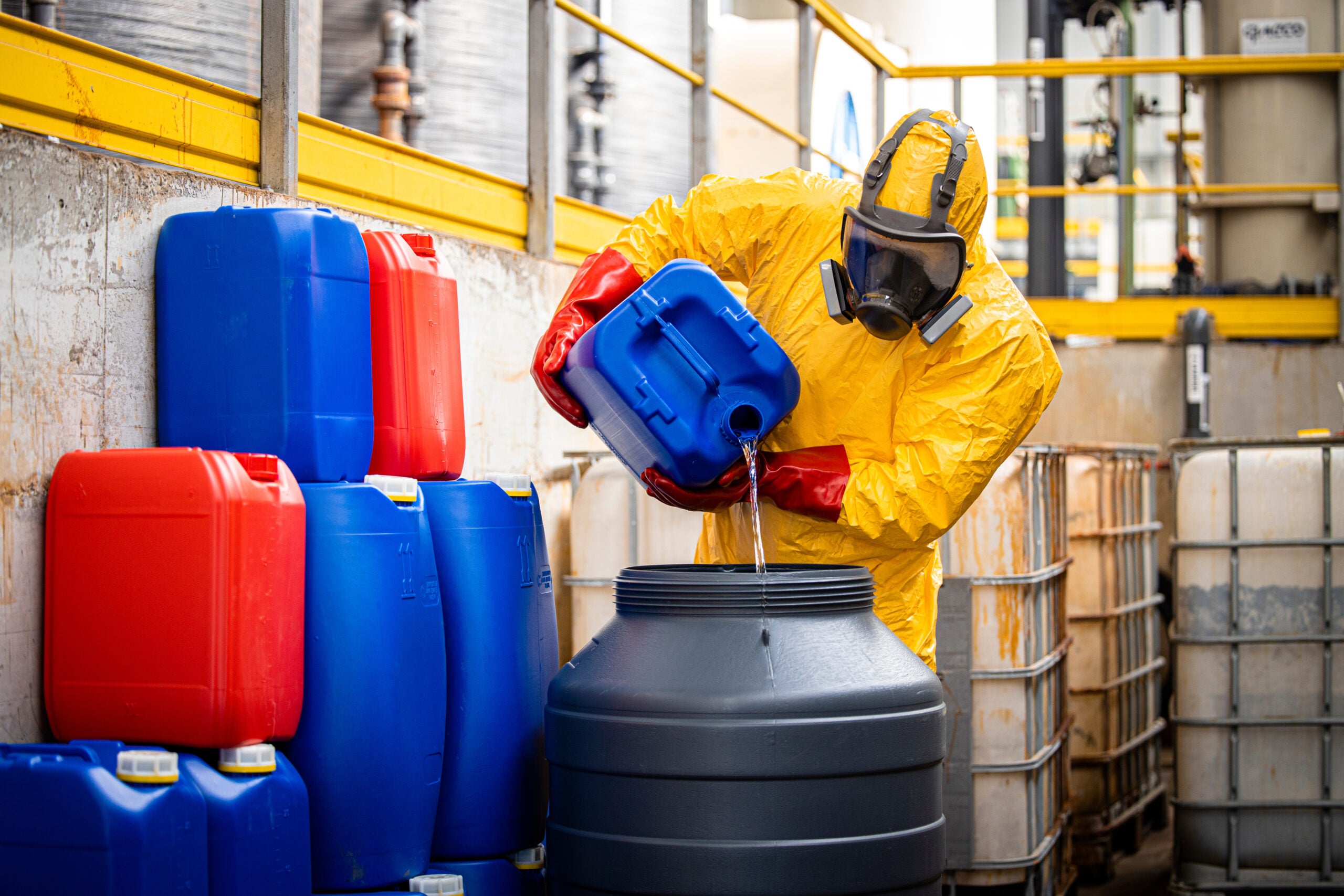 Chemical worker in hazmat suit and full-face respirator making new chemicals for industry.