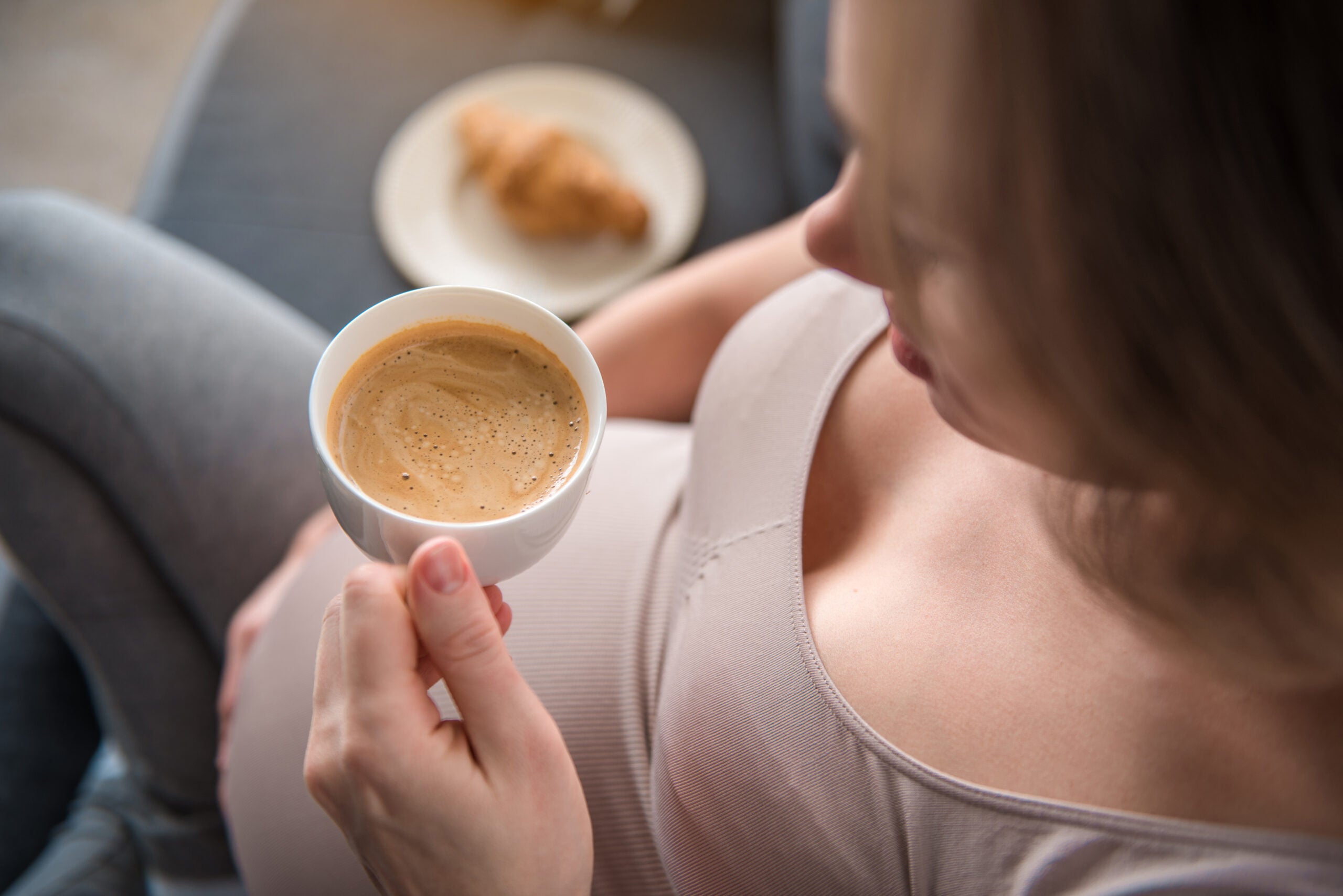 Pregnant woman rests a cup of coffee on her belly.