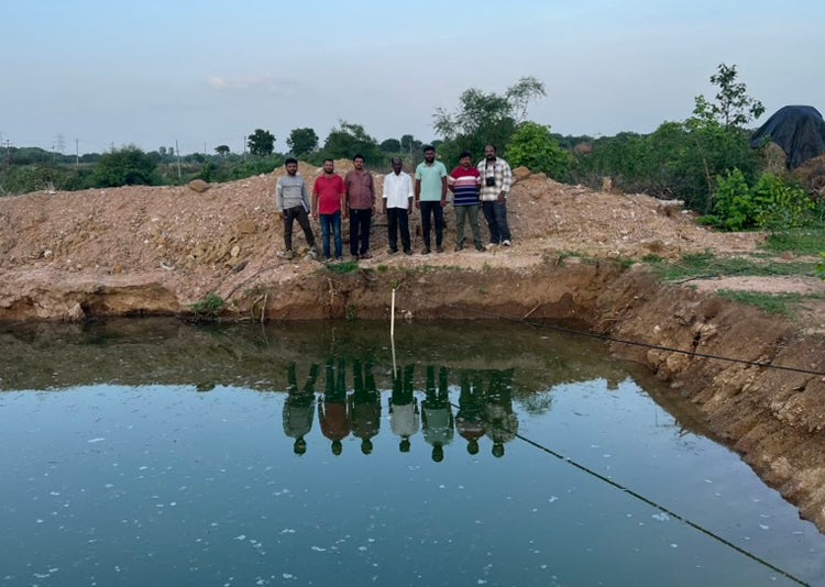 People behind a farm pond with a staff gauge to measure water levels
