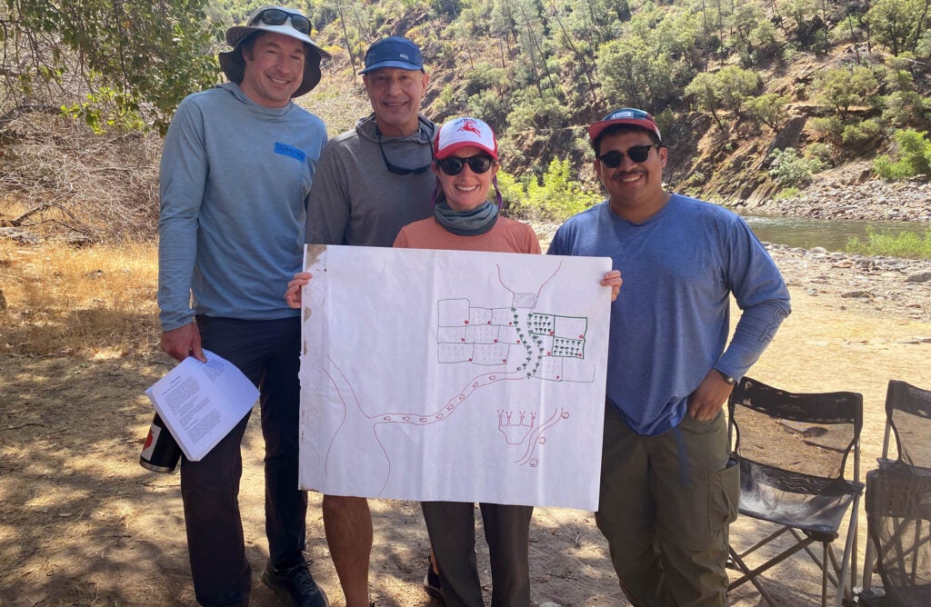 Four people holding up drawing by river.