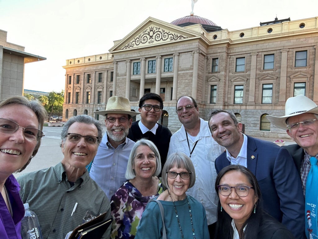 A group of people pose outside of the Arizona state capitol. More details in caption.