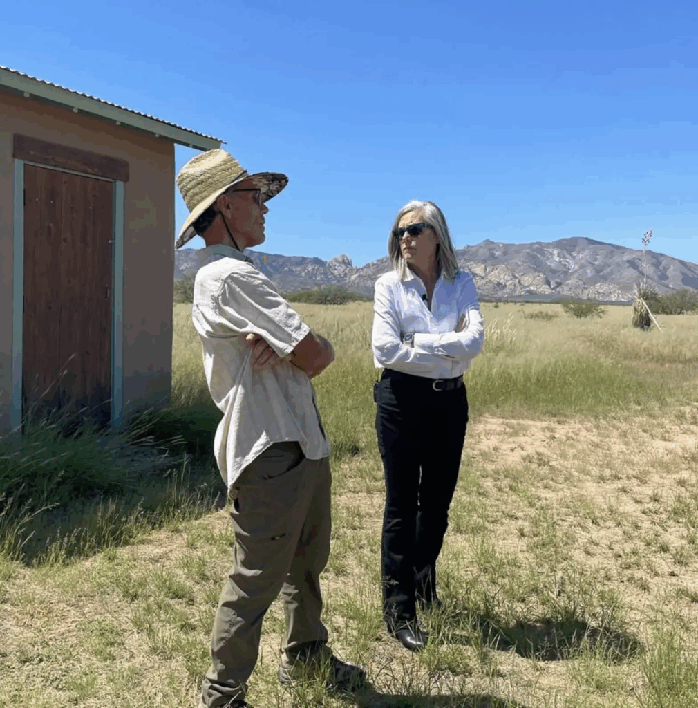 A man and woman talk outside, with mountains behind them. More details in caption.
