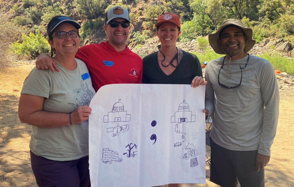 Four people holding up a drawing by the river.
