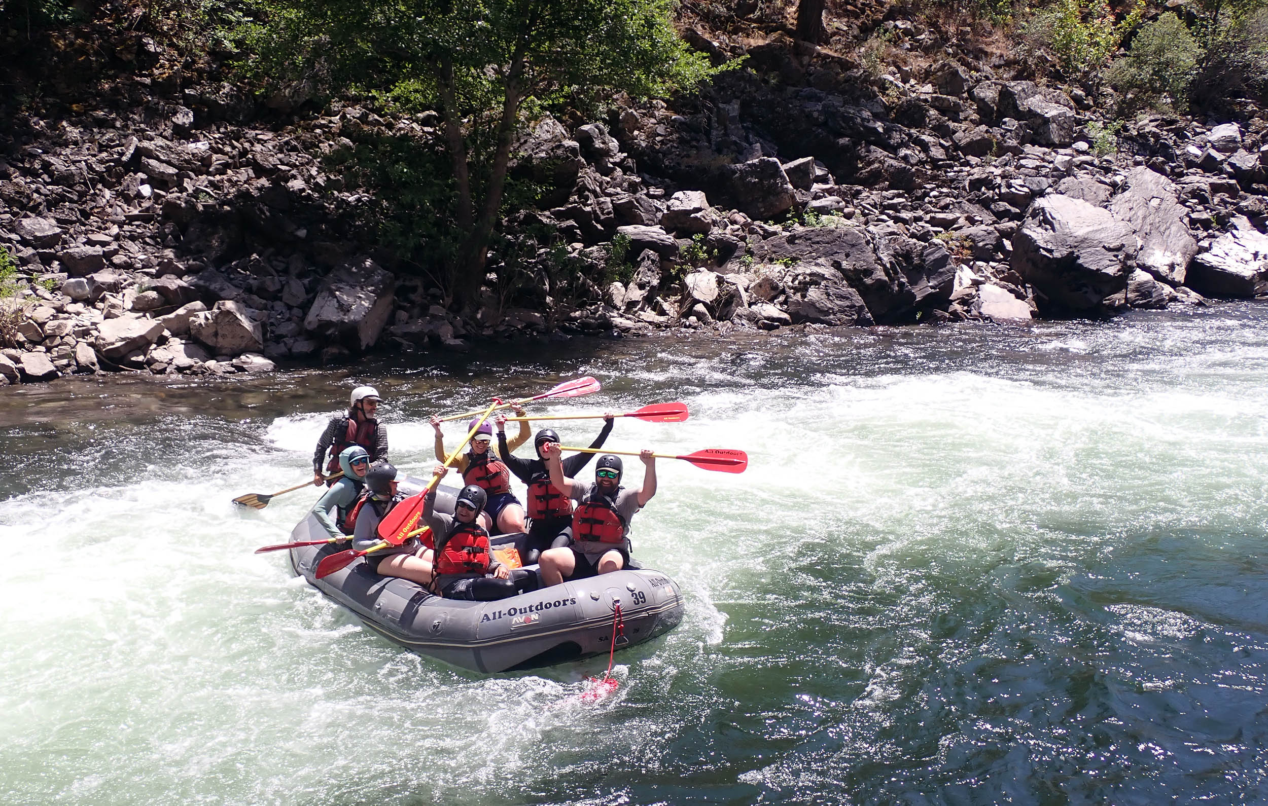 Group in river raft on river holding paddles up in the air.